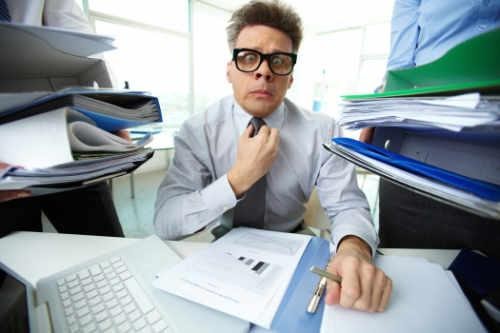 Man in office surrounded by disorganized papers – guilt and shame at work can lead to mental health issues